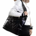 Donna senza volto con un piumino bianco con pelliccia marrone che porta a tracolla una borsa rettangolare in piuma d'oca nera.