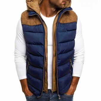 Uomo che indossa un top bianco con sopra un piumino blu e marrone. È rivolto verso il davanti con le mani in tasca.