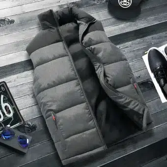 Una giacca trapuntata grigia e nera, senza maniche e senza busto, con tasche semi-aperte con cerniera, stesa su un pavimento a strisce grigio scuro. Ai lati, un berretto nero, una scarpa da ginnastica nera e un po' di targa.
