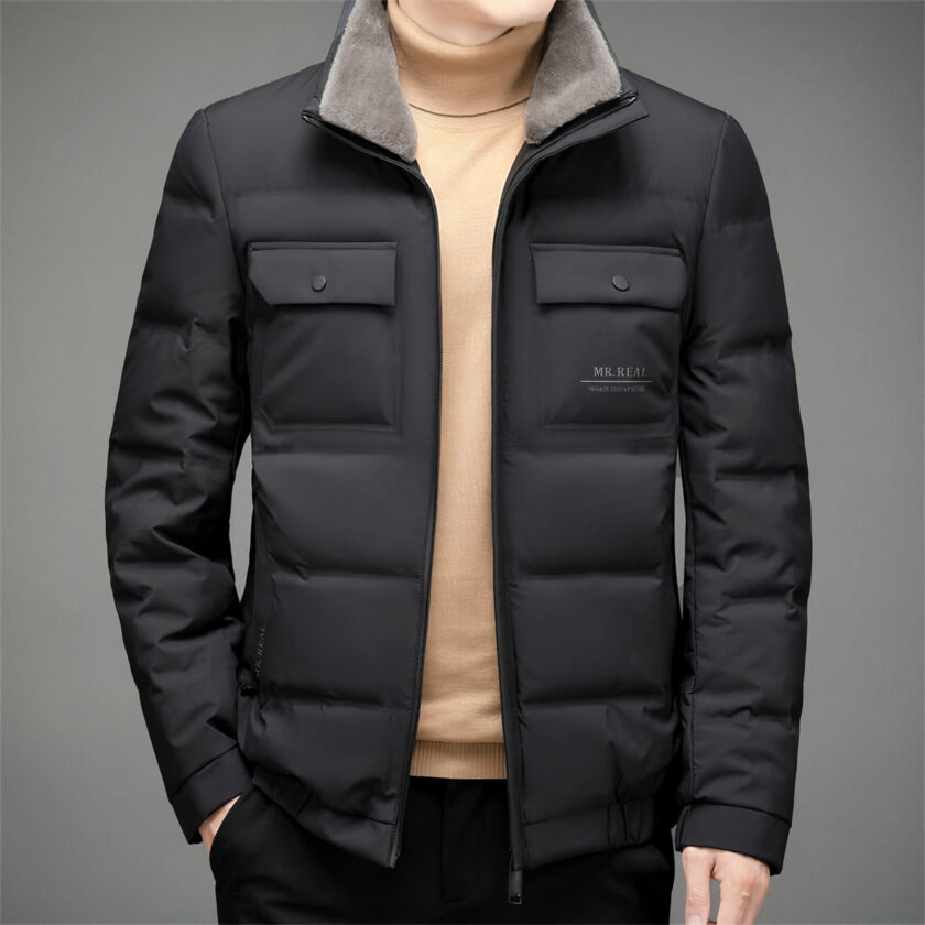 Giacca corta nera opaca con collo in pile e due tasche anteriori con bottoni a pressione sul busto. È indossata semiaperta da un uomo con un maglione beige sotto.