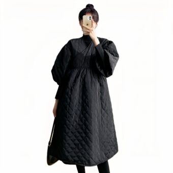 Vediamo una donna con i capelli scuri che indossa un cappotto nero di taglio preppy con un colletto imbottito e avvolgente. Sta scattando una foto a se stessa e non riusciamo a vederne il volto. Lo sfondo è bianco.