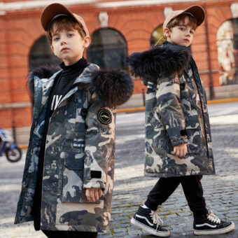 Vediamo un giovane ragazzo di città che indossa un berretto beige, jeans neri e scarpe da ginnastica nere. Indossa anche un piumino con stampa militare e un cappuccio nero bordato di pelliccia.