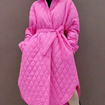 Vediamo una donna che indossa un piumino rosa fucsia con trapuntatura e cintura. Il taglio è a trapezio.