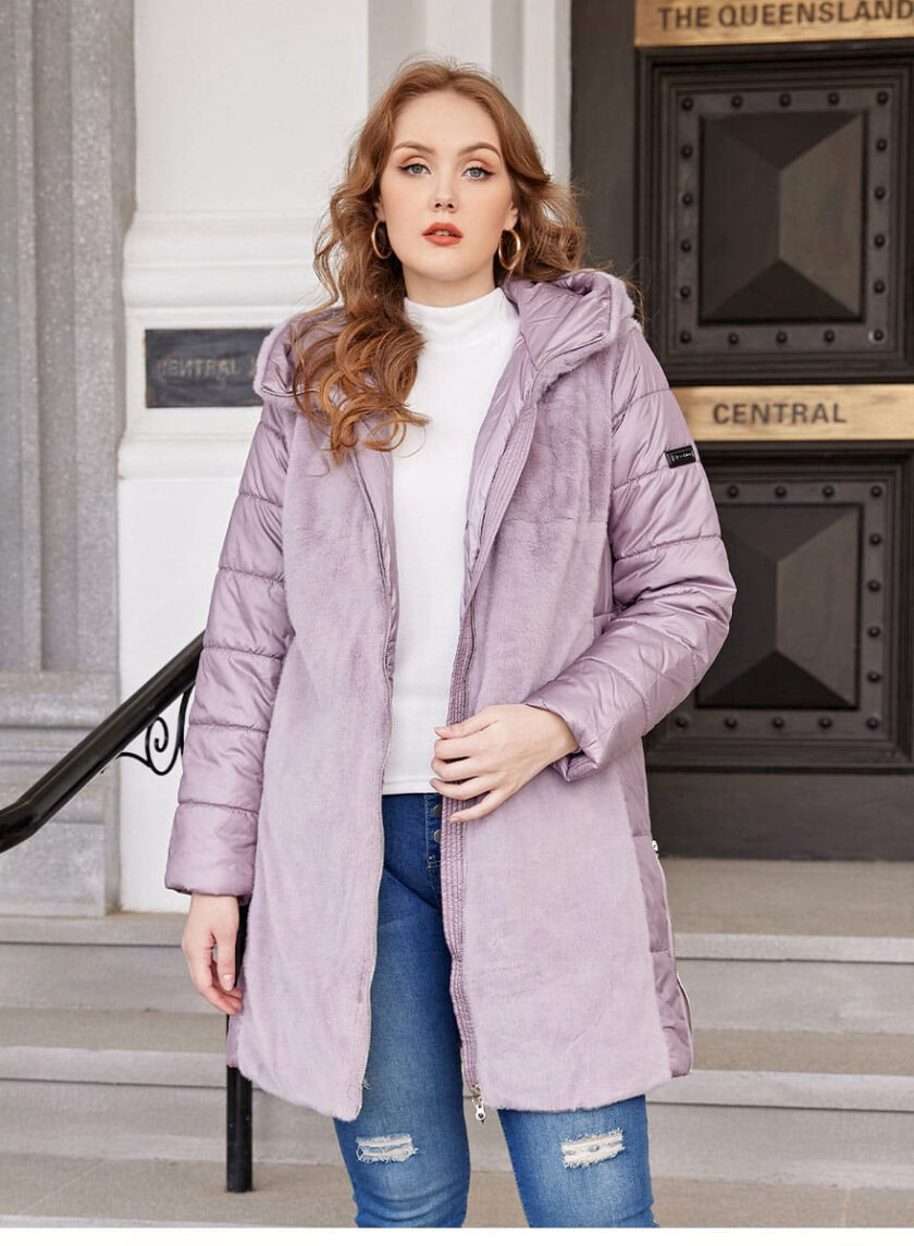 Piumino viola aperto con pelliccia corta sul davanti e maniche trapuntate. È indossato da una donna con lunghi capelli sciolti e ondulati, che sotto indossa un maglione bianco e jeans blu strappati sopra le ginocchia. Sullo sfondo ci sono delle scale con una grande porta nera e oro.