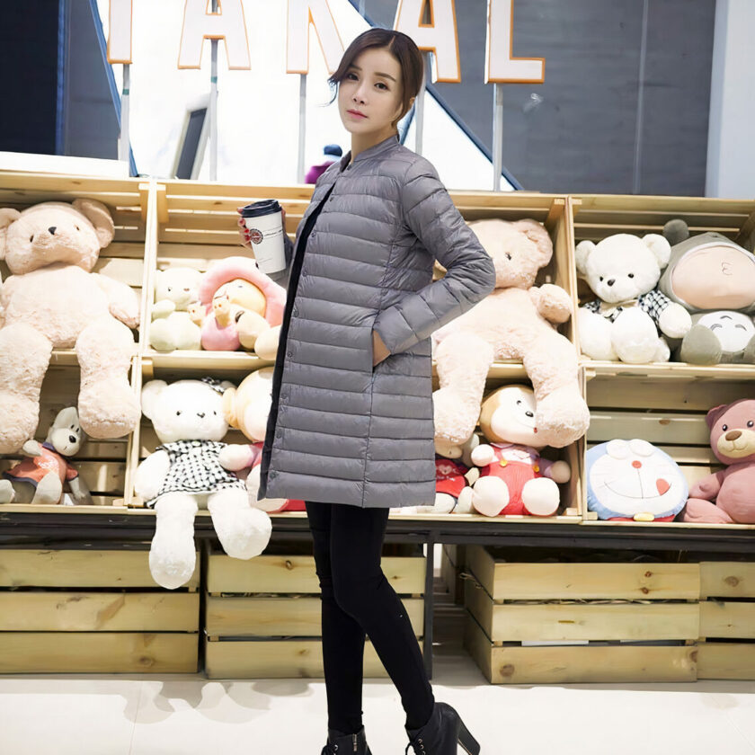 Donna in posa davanti a uno scaffale di peluche con pantaloni neri e piumino grigio.