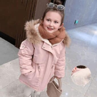 Vediamo una bambina molto carina nell'atrio di un palazzo, che indossa un caldo piumino rosa con un cappuccio foderato di pile e pelliccia.