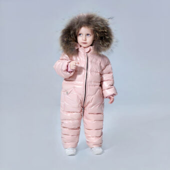 Bambina che indossa un piumino rosa a protezione totale con il cappuccio sulla testa davanti a uno sfondo grigio.