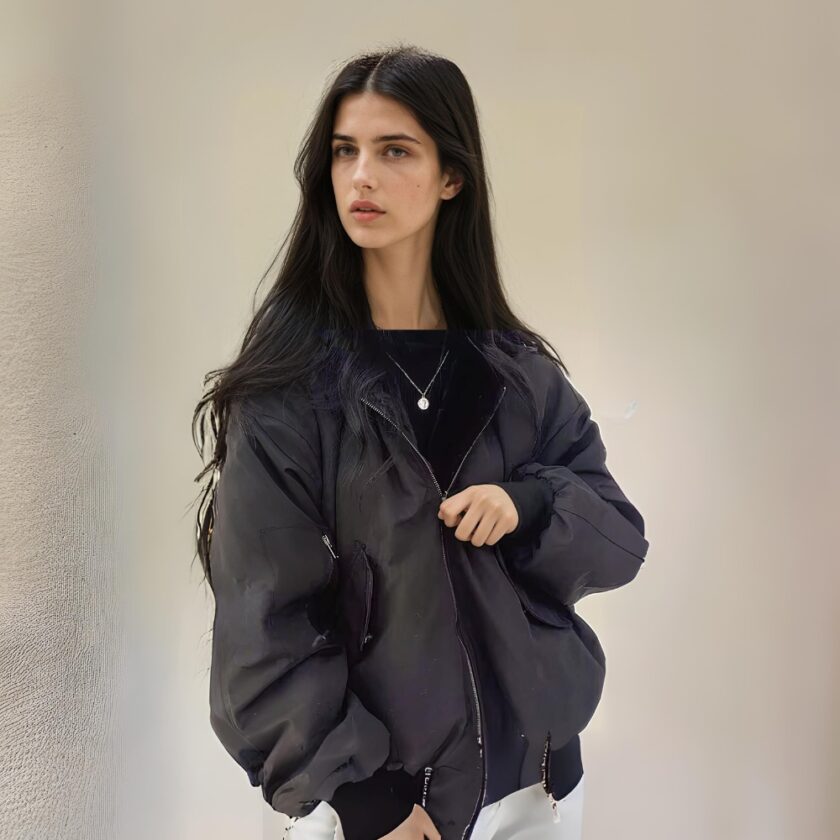 Donna giovane, snella, bruna, con capelli lunghi e sciolti, indossa una giacca nera reversibile. In piedi, con le spalle rivolte a una parete beige.