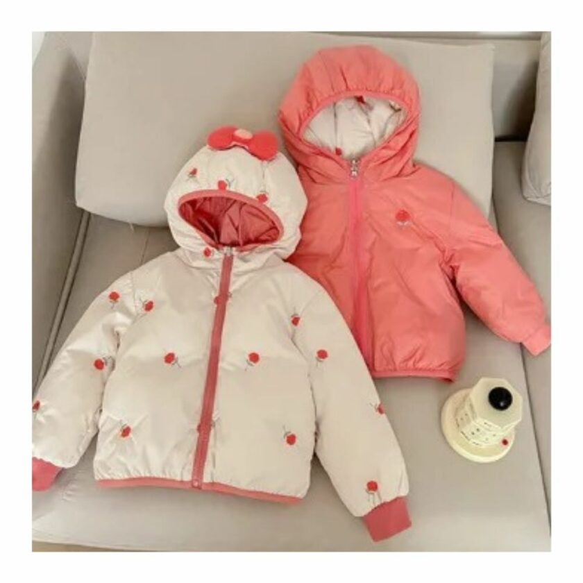 Giacca reversibile per bambine di colore rosa, adagiata su un divano beige.