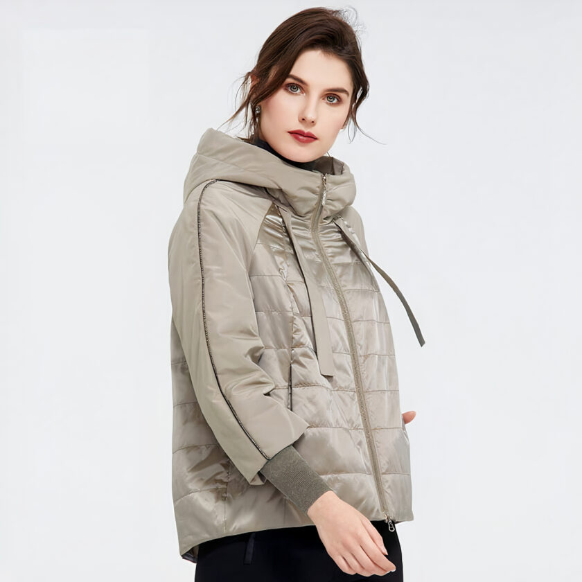 Donna bruna su sfondo grigio che indossa un ampio piumino primaverile beige.