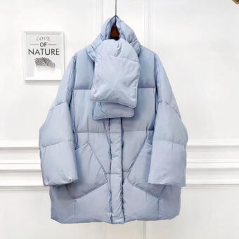 Vediamo un piumino oversize di colore blu chiaro. È presentato su uno sfondo chiaro e minimalista.
