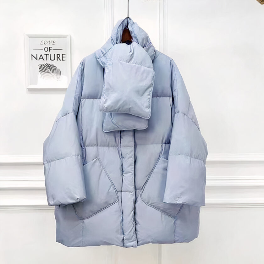 Vediamo un piumino oversize di colore blu chiaro. È presentato su uno sfondo chiaro e minimalista.