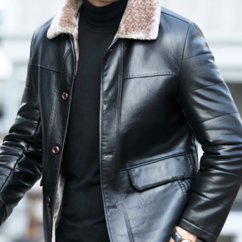 Vediamo il busto di un uomo che cammina per strada. Indossa un maglione nero e un cappotto di pelle con il collo di pelliccia. Ha un aspetto elegante.