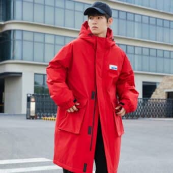 Immagine di un uomo che indossa un piumino rosso di media lunghezza e un berretto blu navy. È in piedi per strada con le mani nelle tasche del piumino.