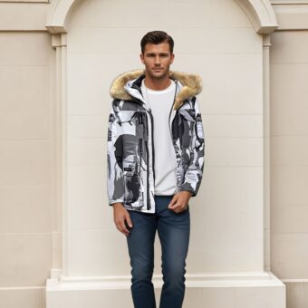 Uomo dai capelli castani che indossa jeans blu scuro, un top bianco e un piumino con motivi mimetici bianchi, grigi e neri e un cappuccio di pelliccia marrone. Alle sue spalle, un muro di pietra beige.