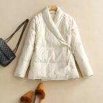 Giacca corta da donna su sfondo beige. Accanto ad essa si intravede una borsa nera.