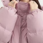 Donna che indossa un piumino rosa, con solo la parte superiore del corpo visibile e le mani sul colletto