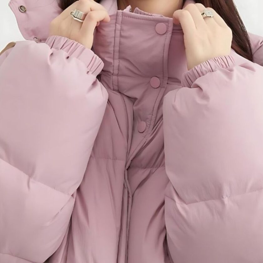 Donna che indossa un piumino rosa, con solo la parte superiore del corpo visibile e le mani sul colletto