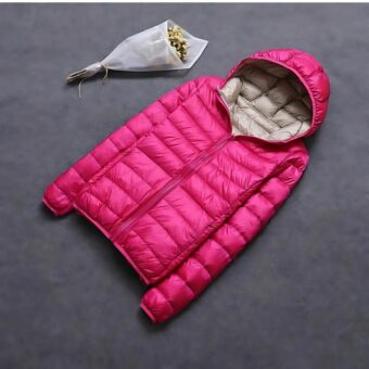 Ampia giacca da donna reversibile di colore rosa acceso, stesa con un cappuccio beige, accompagnata da un bouquet di fiori di carta bianchi.