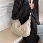 si vede una donna che porta a tracolla una borsa da donna con piumino a mezzaluna la borsa è beige