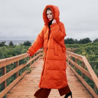 Piumino arancione da donna in taglie forti, con cappuccio in rilievo e piuma d'anatra. Vista di una donna che indossa questo lungo piumino, ideale per valorizzare le figure formose in inverno con un tocco di fantasia e calore.